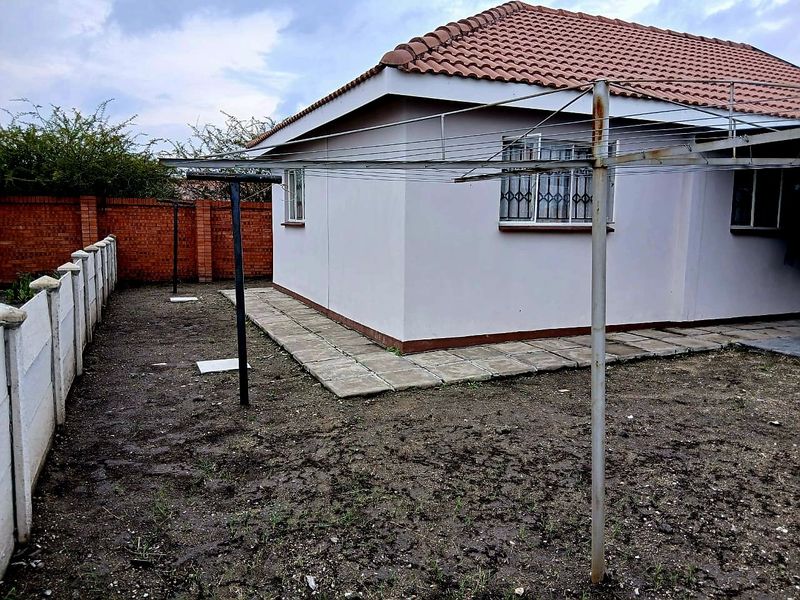 Rear exterior view of the house featuring a tiled roof, concrete paving, and a large metal washing line set within a fenced yard.