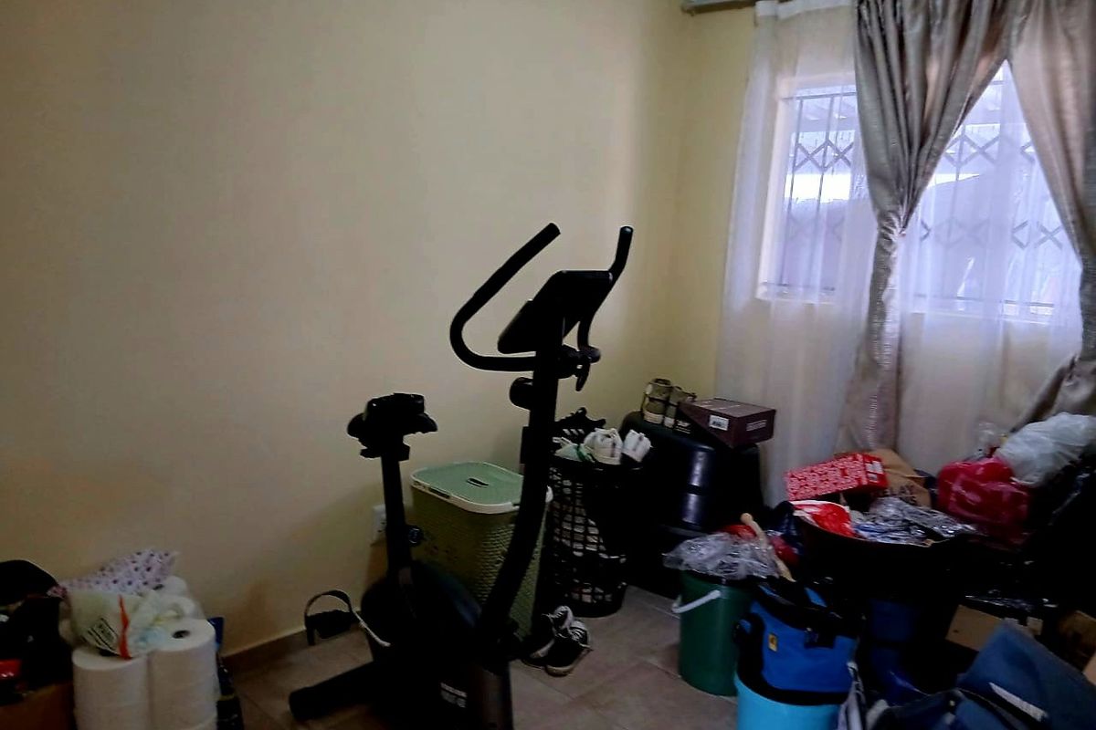 A bedroom featuring tiled flooring and a window fitted with security bars, currently utilized as a multi-purpose storage and exercise space.