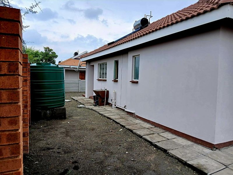 Rear exterior view of the house featuring a paved walkway, solar water heating system, and a large water storage tank.