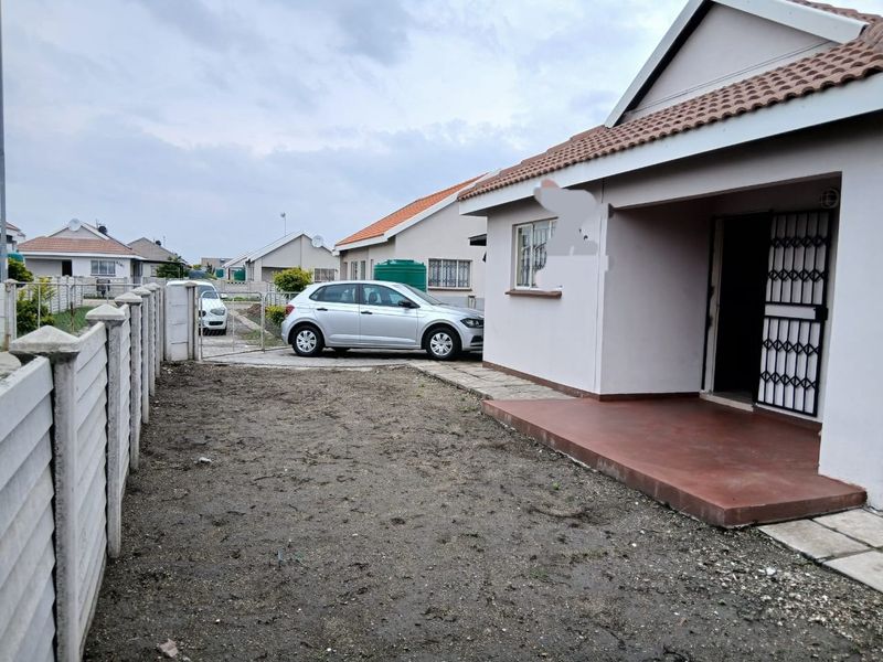 Front view of a residential property featuring a paved entrance, security gate, and an unlandscaped yard area with a precast boundary wall.