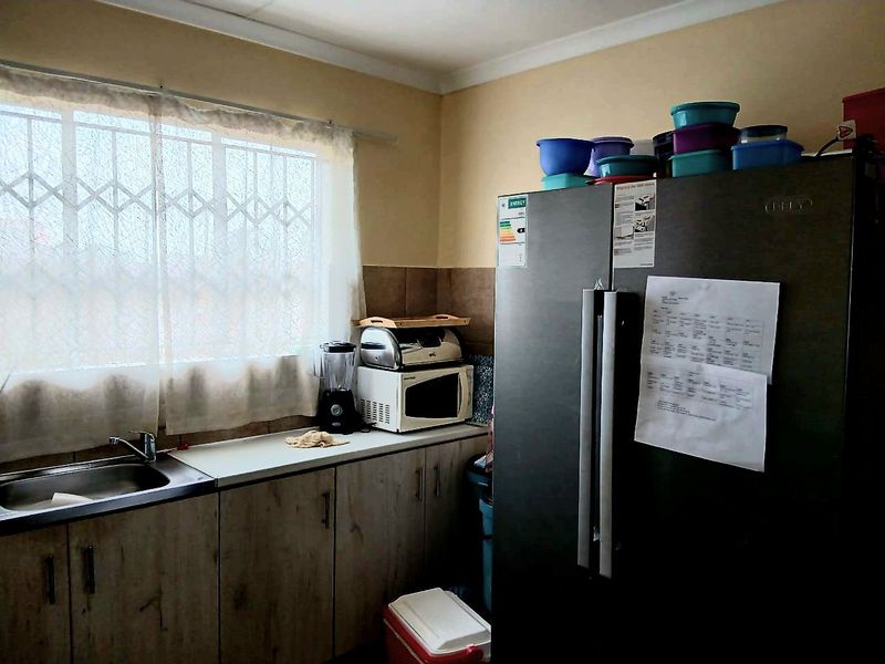 A functional kitchen area featuring built-in cabinetry, a stainless steel sink, and a tiled backsplash, with security bars installed on the window.