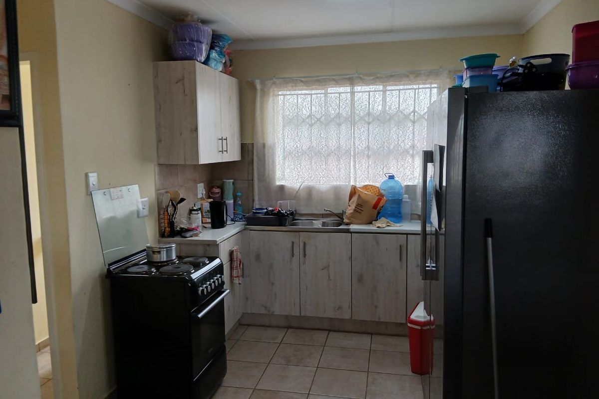 A functional kitchen featuring light-toned cabinetry, tiled flooring, a double sink, and security bars on the window.