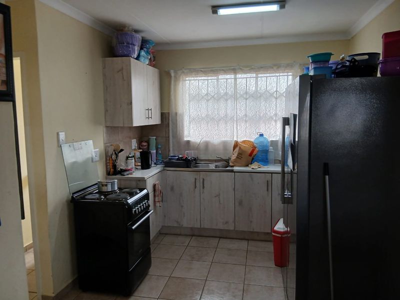 A functional kitchen featuring light-toned cabinetry, tiled flooring, a double sink, and security bars on the window.