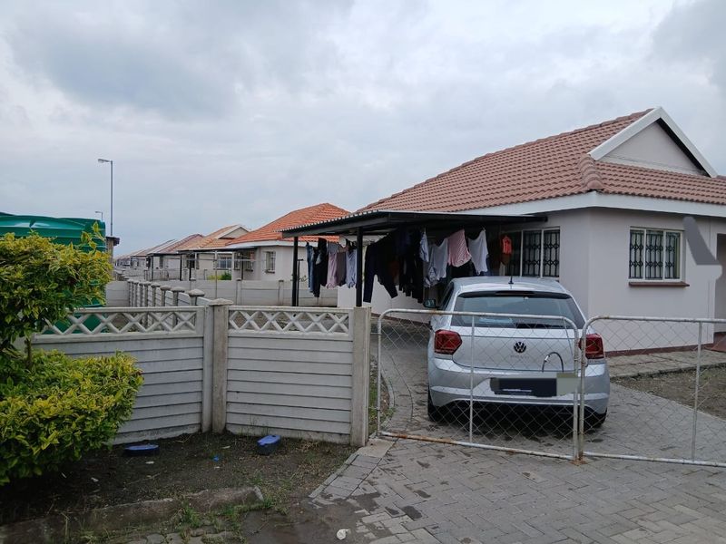 Front exterior view of a residential house featuring a tiled roof, paved driveway, carport, and precast concrete boundary wall with security gate.