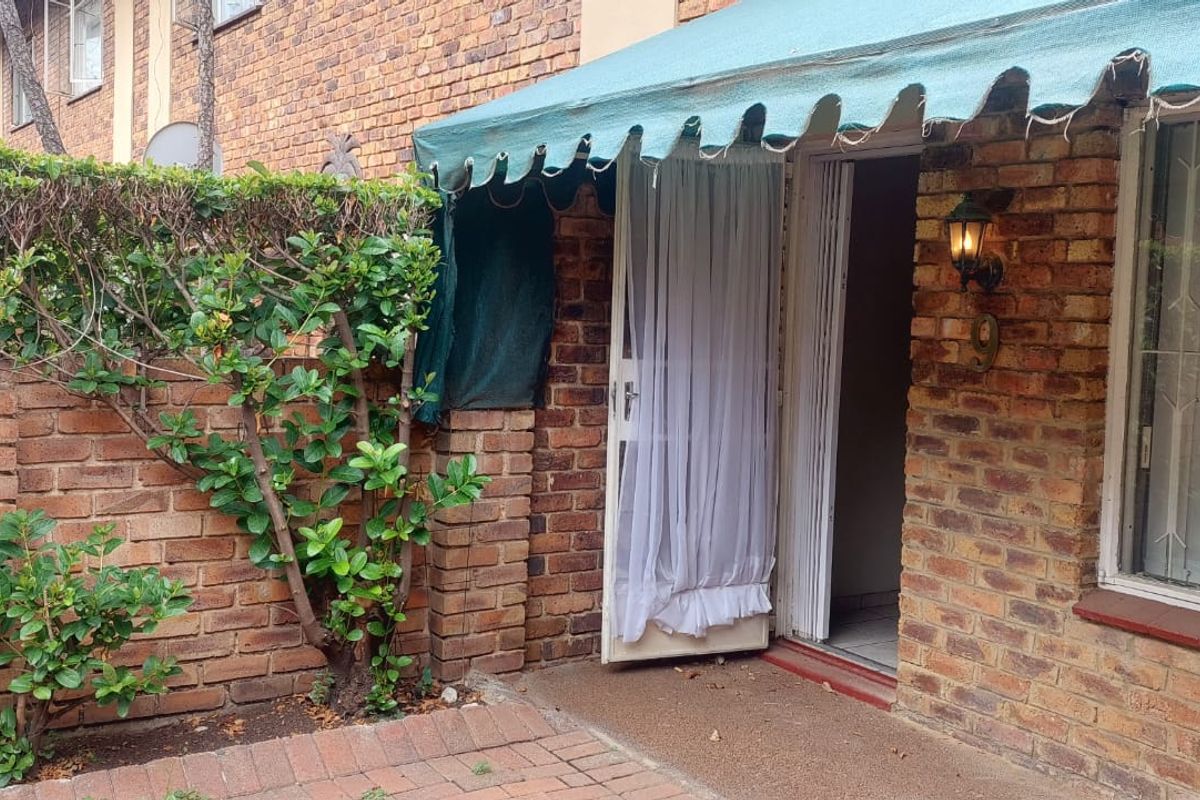 Rear exterior view of the townhouse featuring a brick facade, paved patio area, and a fabric awning over the entrance.