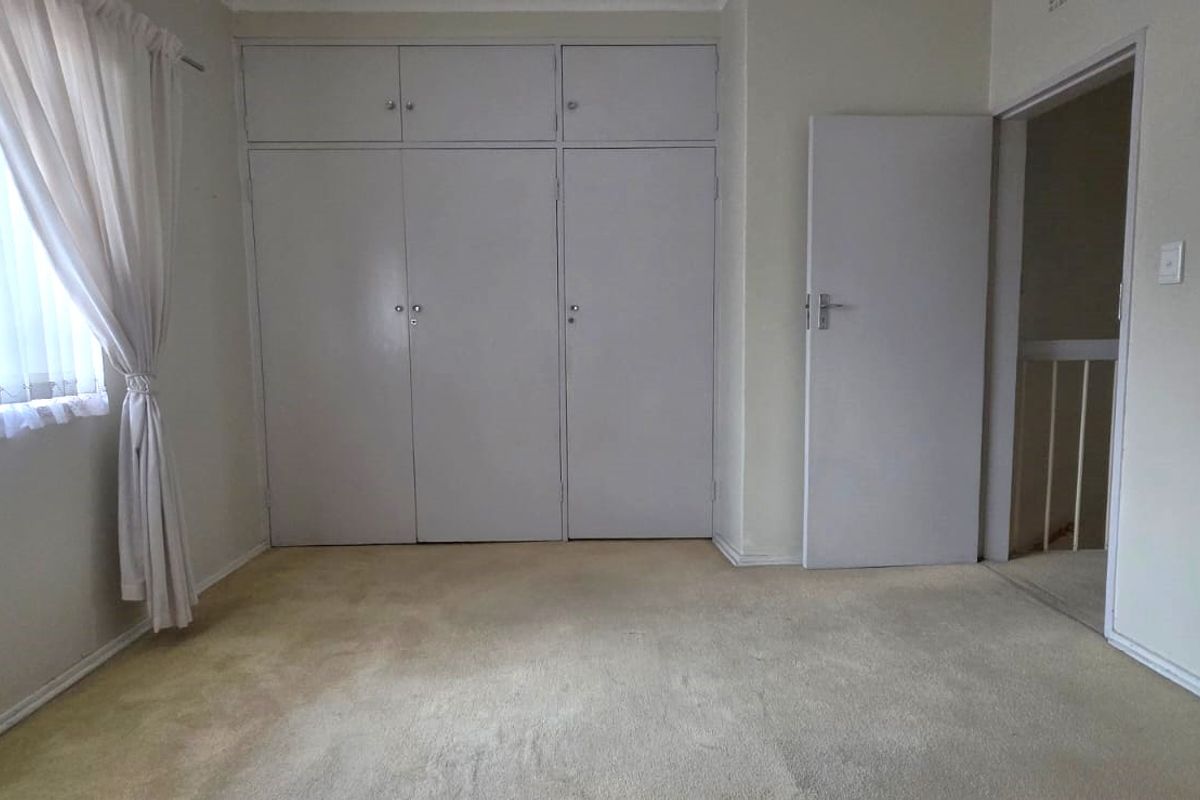 A vacant bedroom featuring built-in cupboards, carpeted flooring, and vertical blinds, offering a blank canvas for personalization.