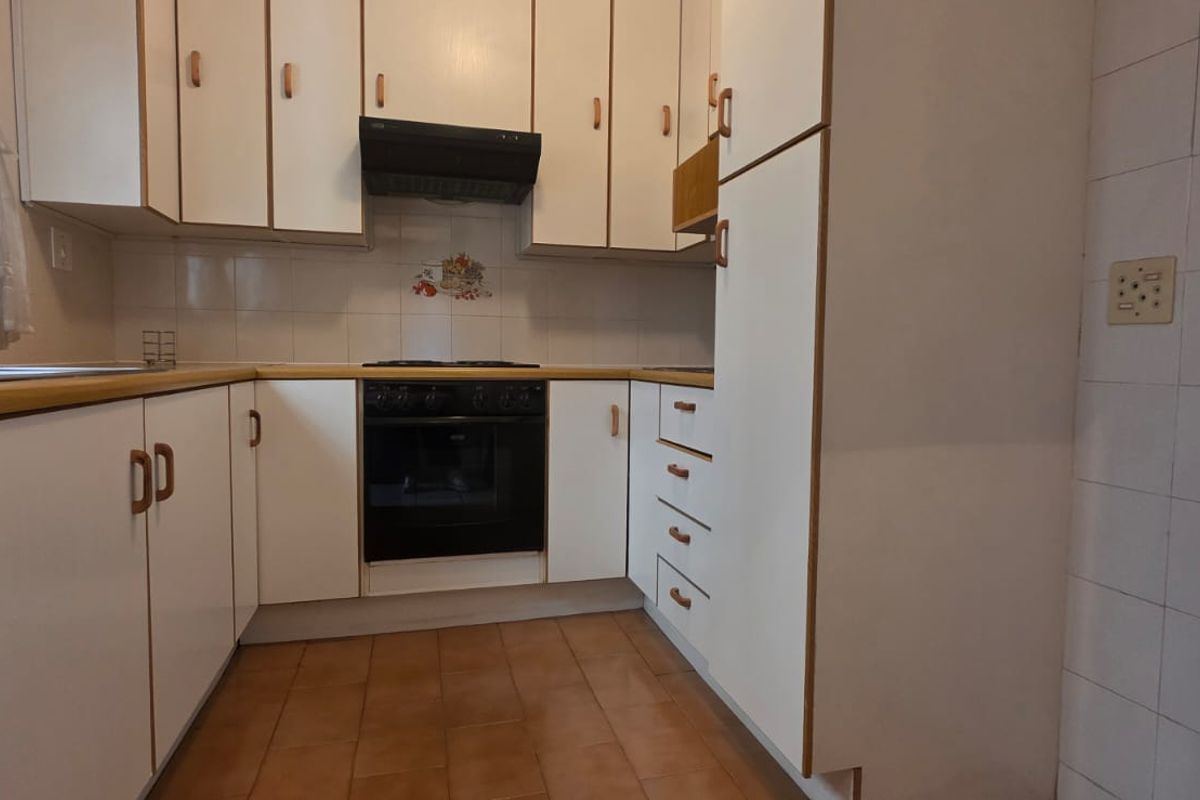 A functional kitchen featuring white built-in cabinetry, laminate countertops, a built-in oven with extractor fan, and tiled flooring.