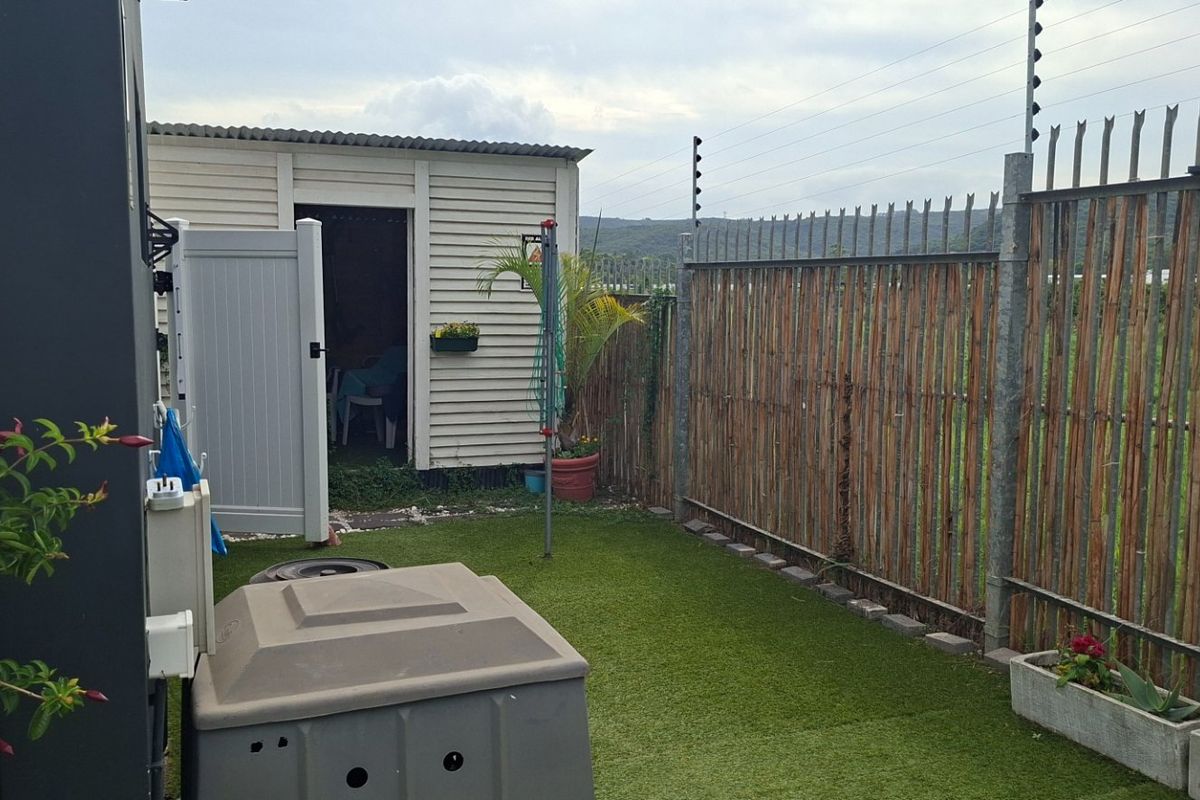A compact rear garden area featuring artificial turf, a utility shed, and perimeter security with electric fencing and bamboo screening.