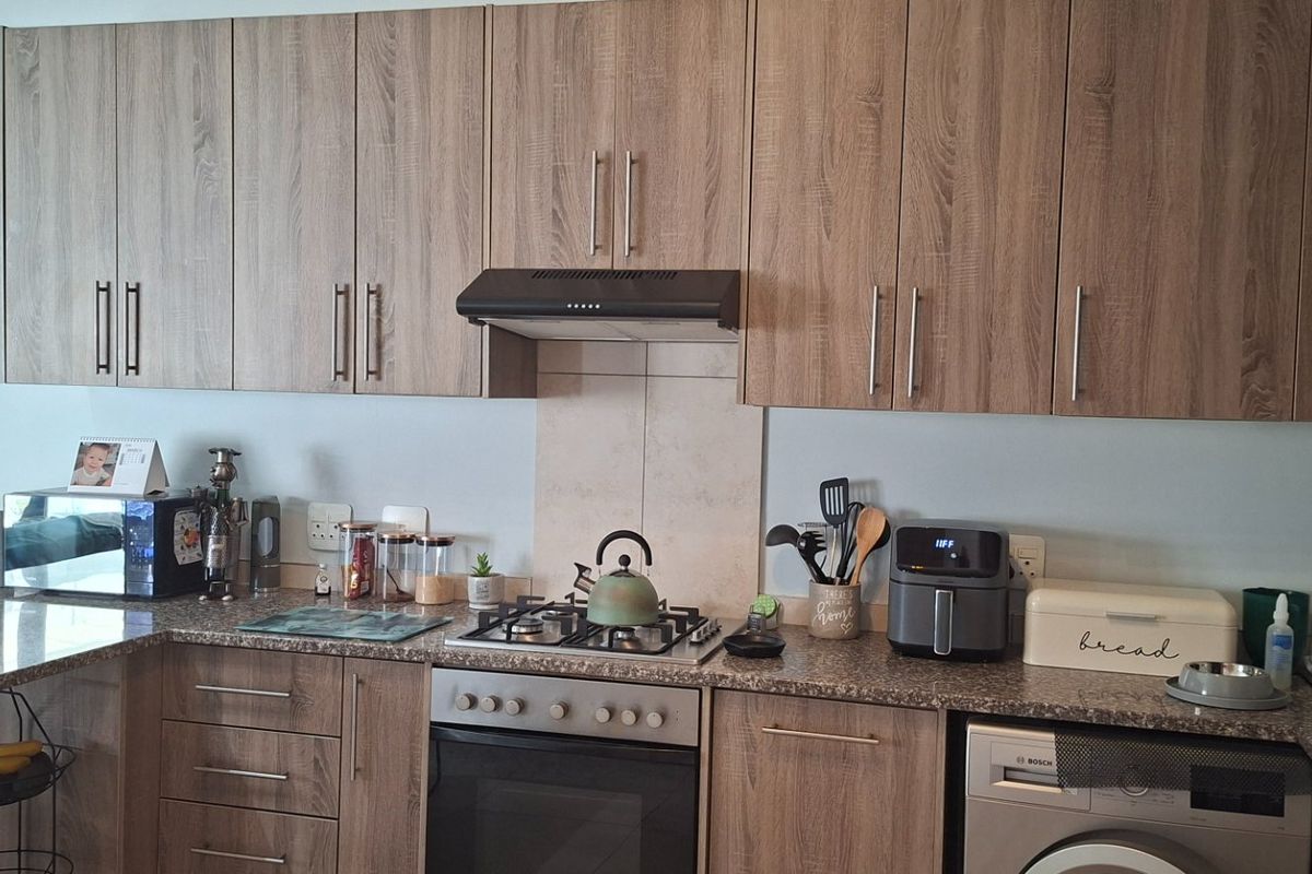 A functional kitchen featuring wood-look laminate cabinetry, granite countertops, a gas hob with extractor fan, and an integrated washing machine.
