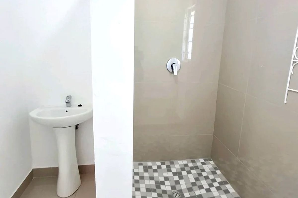A clean, modern bathroom featuring a pedestal basin and a walk-in shower with neutral wall tiles and a decorative mosaic floor.