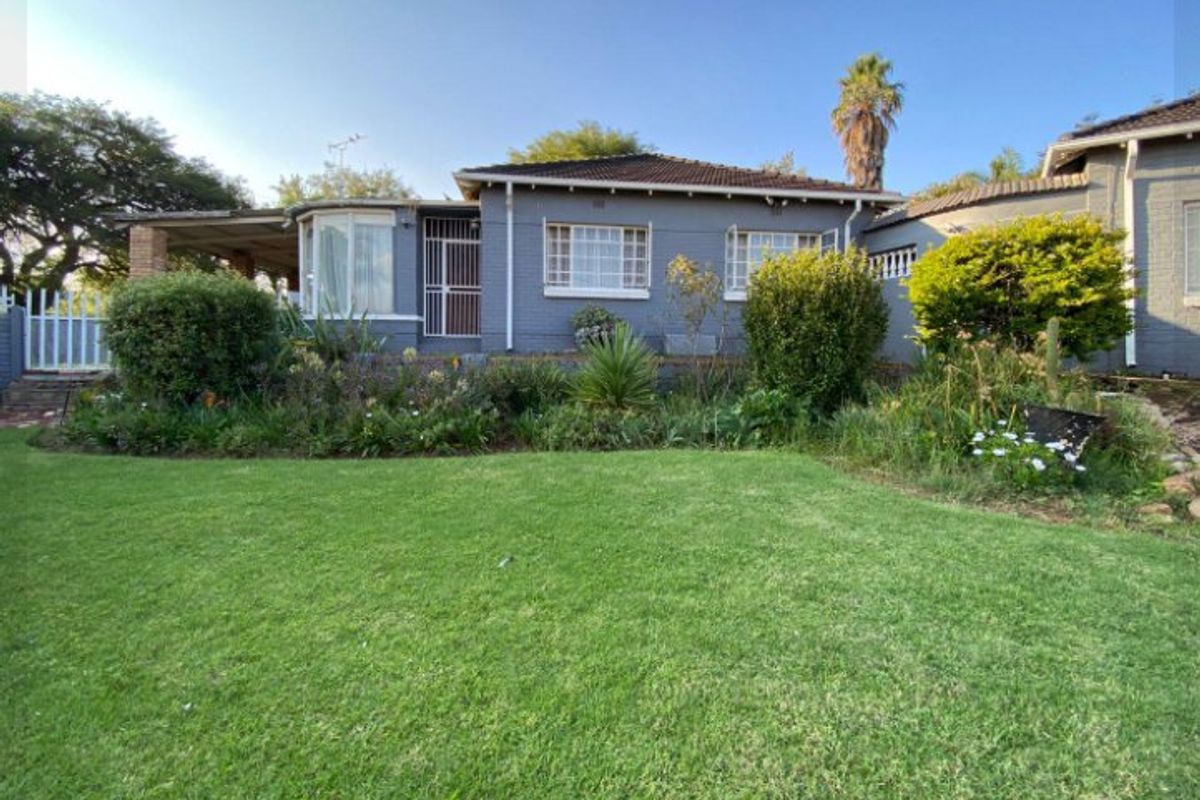 Rear view of the house featuring a brick facade, tiled roof, and a covered patio overlooking a well-maintained garden.