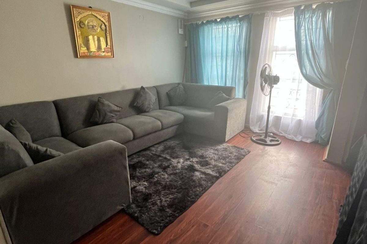 A living room featuring dark wood-look laminate flooring, recessed ceiling lighting, and decorative coving, providing a functional and neutral living space.