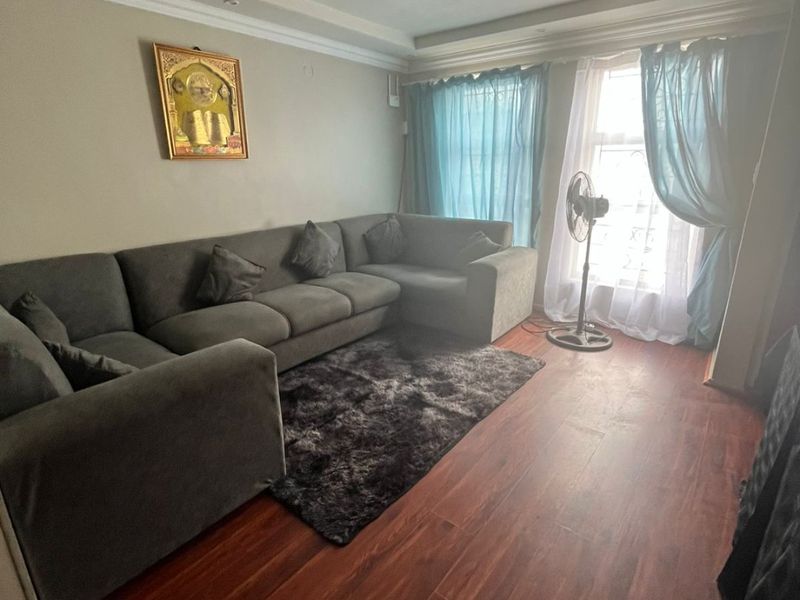 A living room featuring dark wood-look laminate flooring, recessed ceiling lighting, and decorative coving, providing a functional and neutral living space.