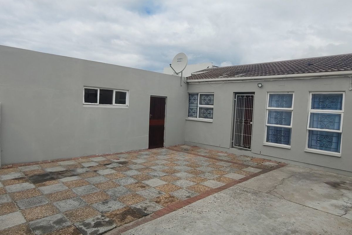 Rear exterior view of the property featuring a paved patio area, security gates, and aluminium window frames.