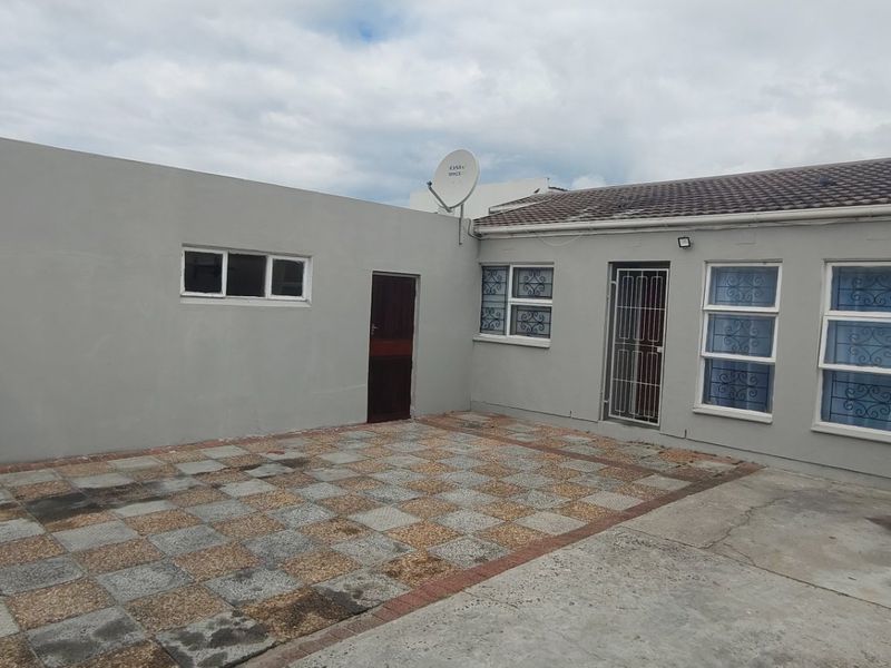 Rear exterior view of the property featuring a paved patio area, security gates, and aluminium window frames.