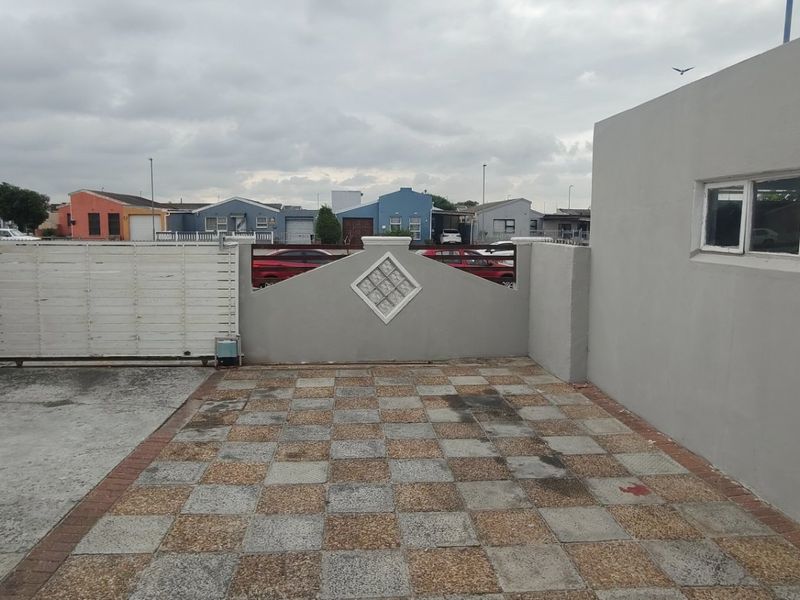 A paved rear courtyard area featuring a boundary wall with a sliding gate and decorative glass block insert.