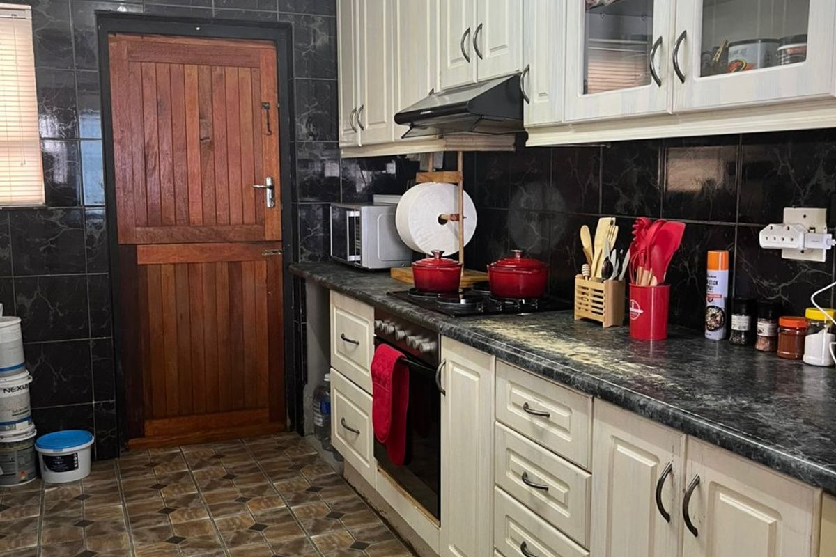 A functional kitchen featuring cream-colored cabinetry, dark marble-effect countertops, black tiled backsplash, and a traditional wooden stable door.
