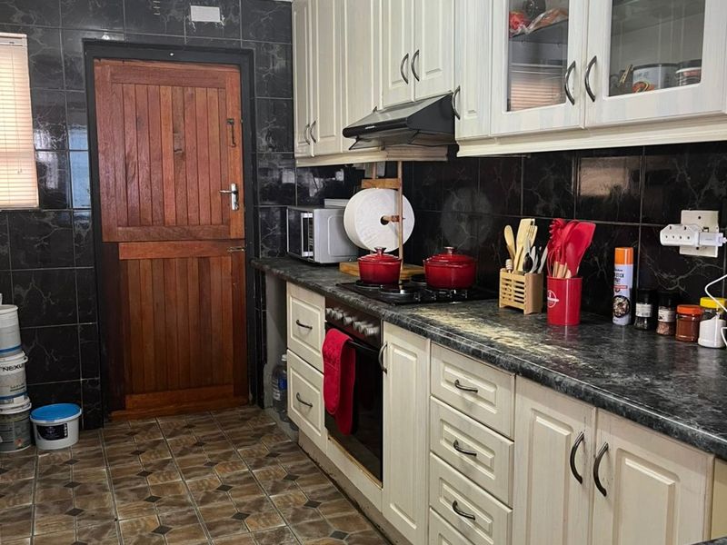 A functional kitchen featuring cream-colored cabinetry, dark marble-effect countertops, black tiled backsplash, and a traditional wooden stable door.