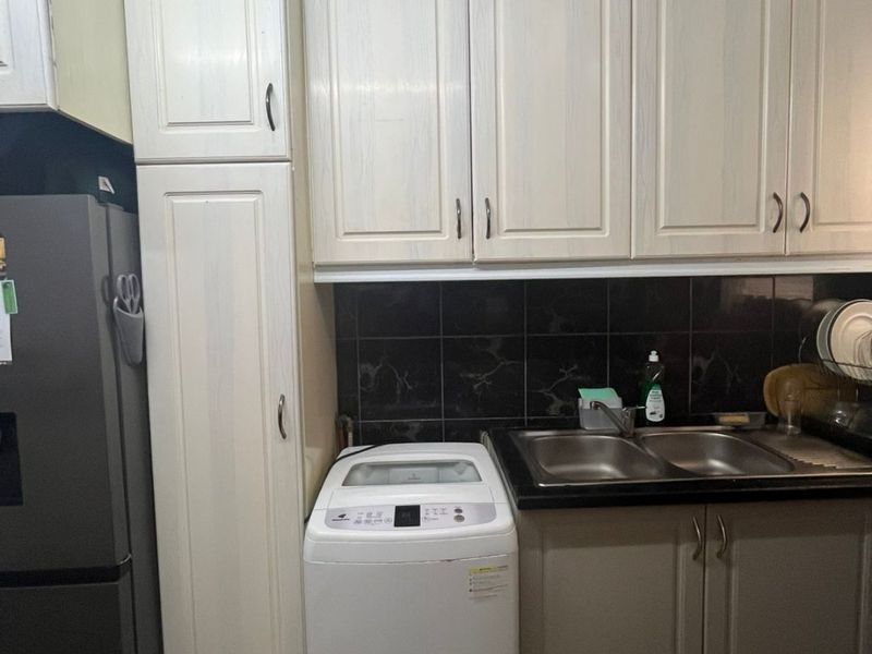 A functional laundry area featuring built-in cabinetry, a double bowl sink, and tiled backsplash, providing practical utility space.