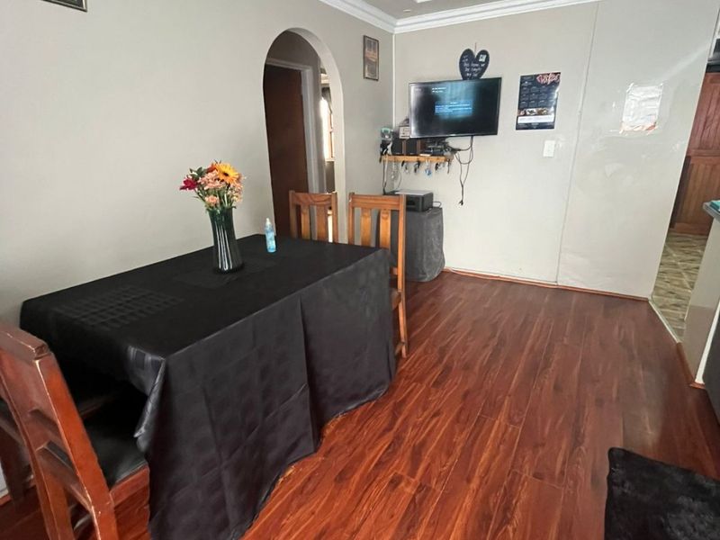 A dining area featuring warm-toned laminate flooring, coved ceiling details, and a classic archway leading to an adjacent room.