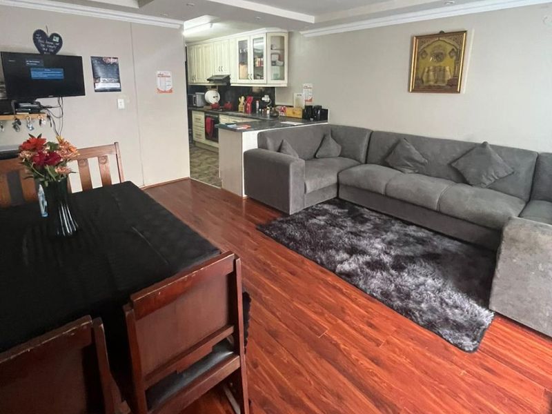 Open plan living and dining area featuring laminate flooring and a connected kitchen with built-in cabinetry and countertop space.