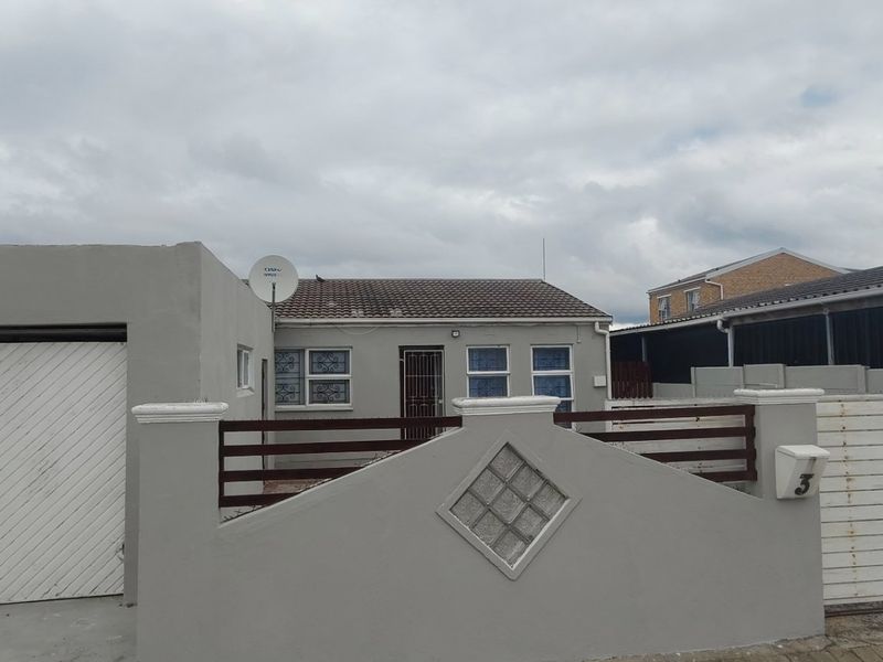 Front exterior view of a single-story house featuring a garage, boundary wall with security gate, and tiled roof.