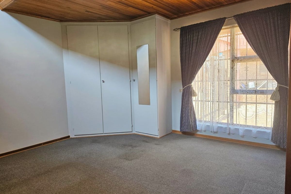 A vacant bedroom featuring built-in cupboards, a timber-paneled ceiling, and carpeted flooring, with security bars installed on the window.