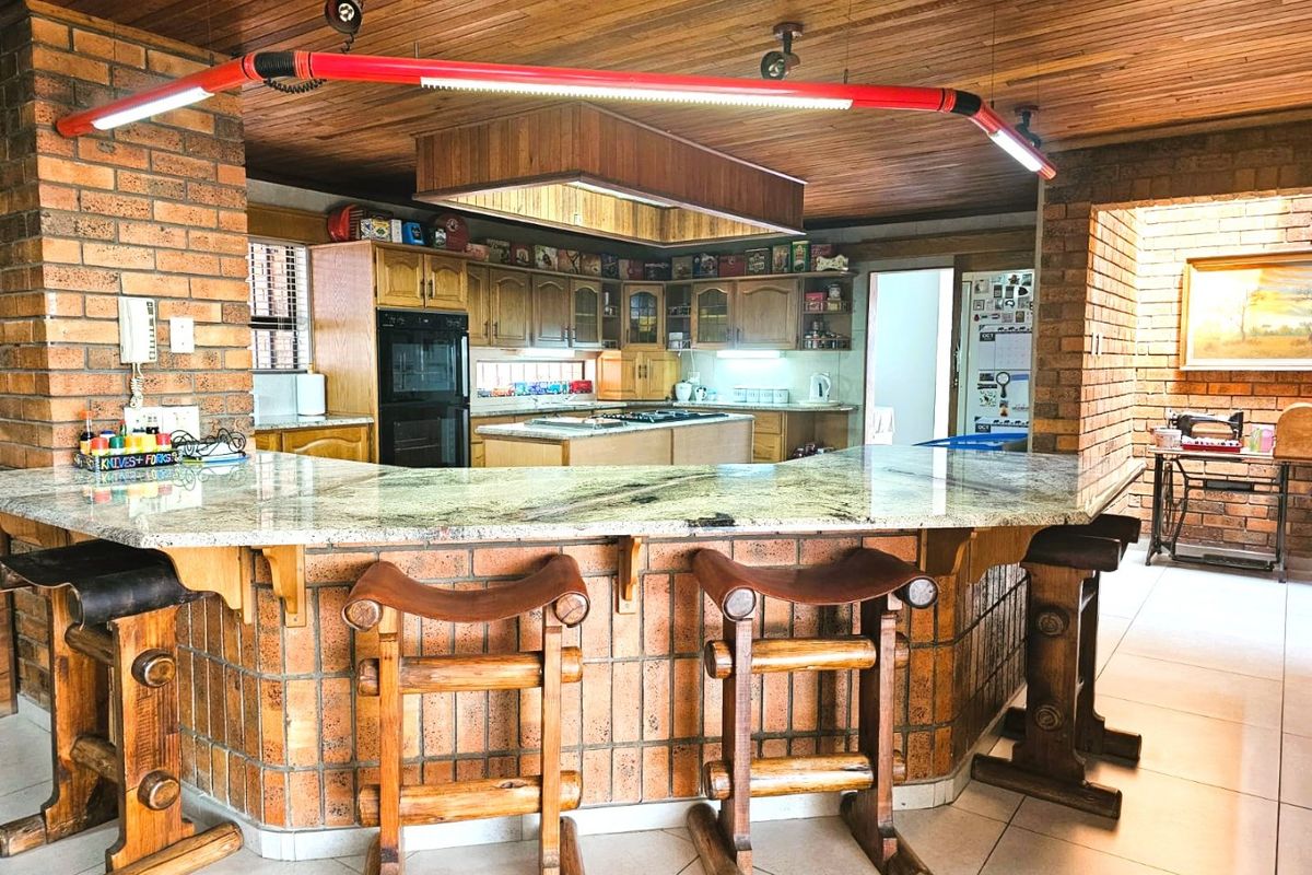 Spacious kitchen featuring a large brick breakfast bar with granite countertops, timber ceiling, and built-in appliances, offering a rustic and functional cooking space.