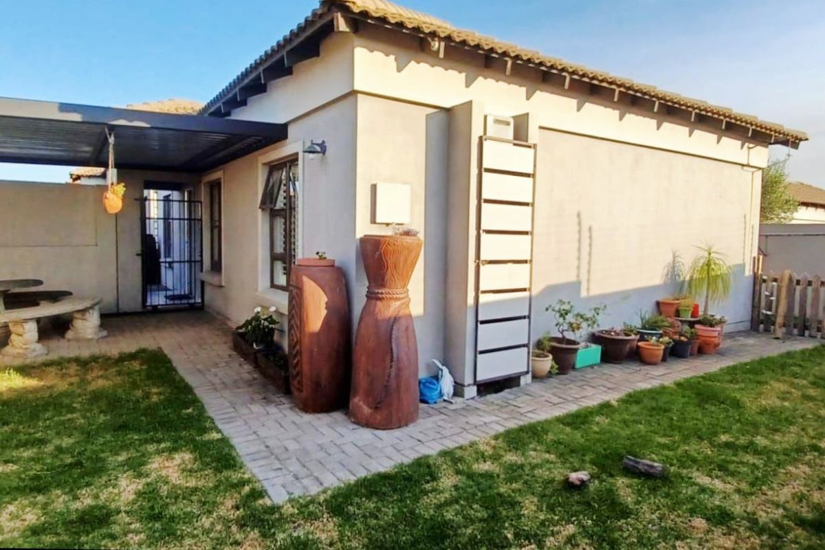 Rear view of the townhouse featuring a covered patio area, paved walkway, and a private garden space.