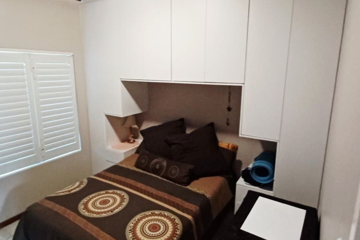 A compact bedroom featuring floor-to-ceiling built-in cupboards and white plantation shutters, providing efficient storage and natural light control.