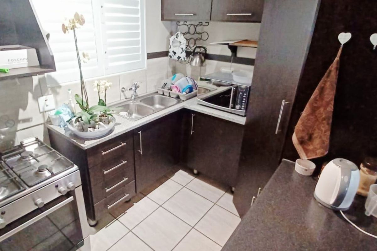 Compact kitchen featuring dark cabinetry, stainless steel sink, gas stove with oven, and tiled flooring, offering a functional workspace.