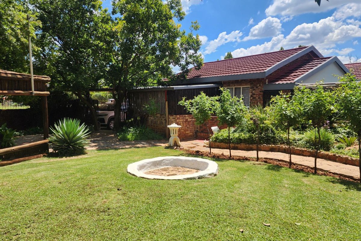 A well-maintained rear garden featuring a central fire pit, established trees, and a paved walkway leading to the main building structure.