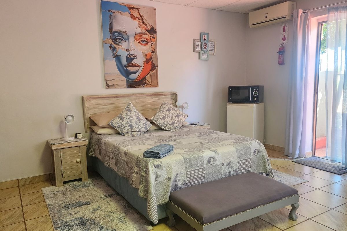 A functional bedroom suite featuring tiled flooring, a wall-mounted air conditioning unit, and direct access to an outdoor area.