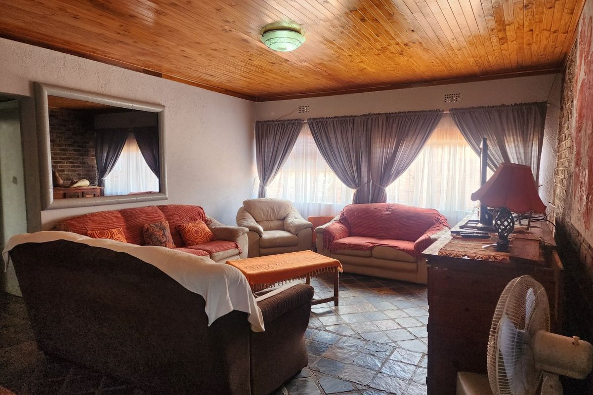 A living room featuring a rustic timber-clad ceiling, stone-tiled flooring, and a large wall-mounted mirror, offering a traditional and cozy atmosphere.