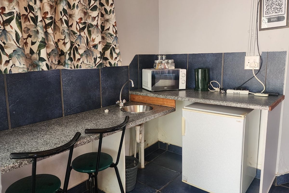 Compact kitchenette area featuring a small sink, granite-look countertop, and tiled splashback, suitable for basic food preparation and storage.