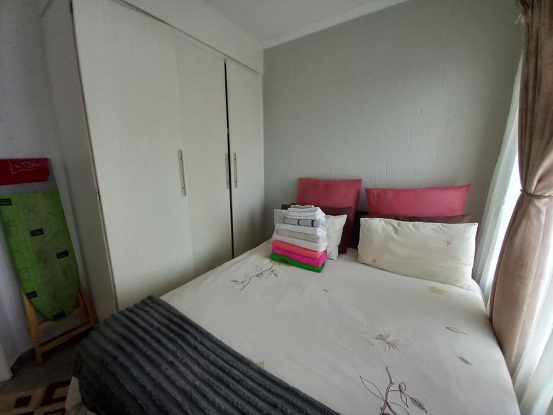 A compact bedroom featuring a built-in wardrobe with white cabinetry and neutral wall finishes.