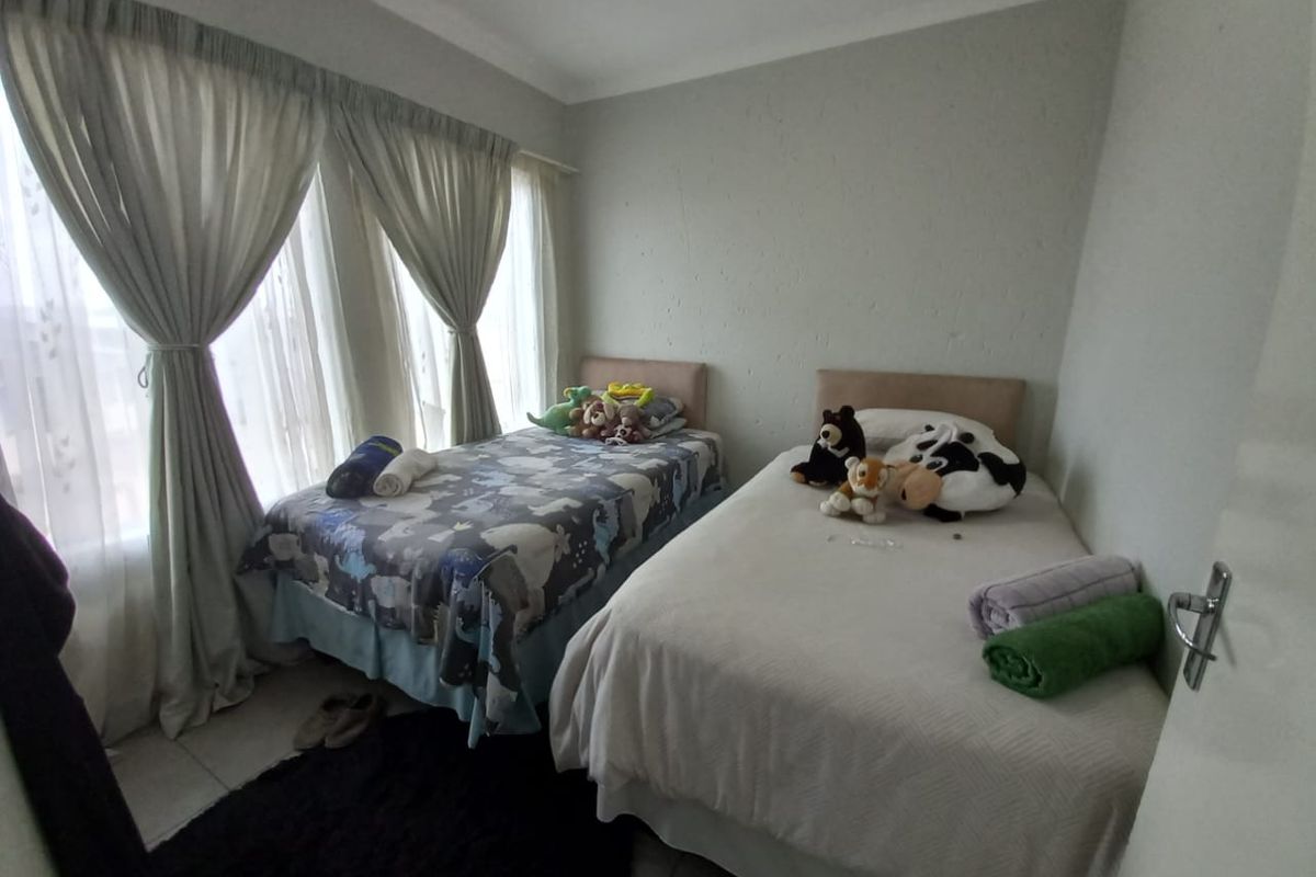 A functional bedroom featuring tiled flooring, coved ceilings, and large windows with curtain treatments, providing a comfortable space for rest.