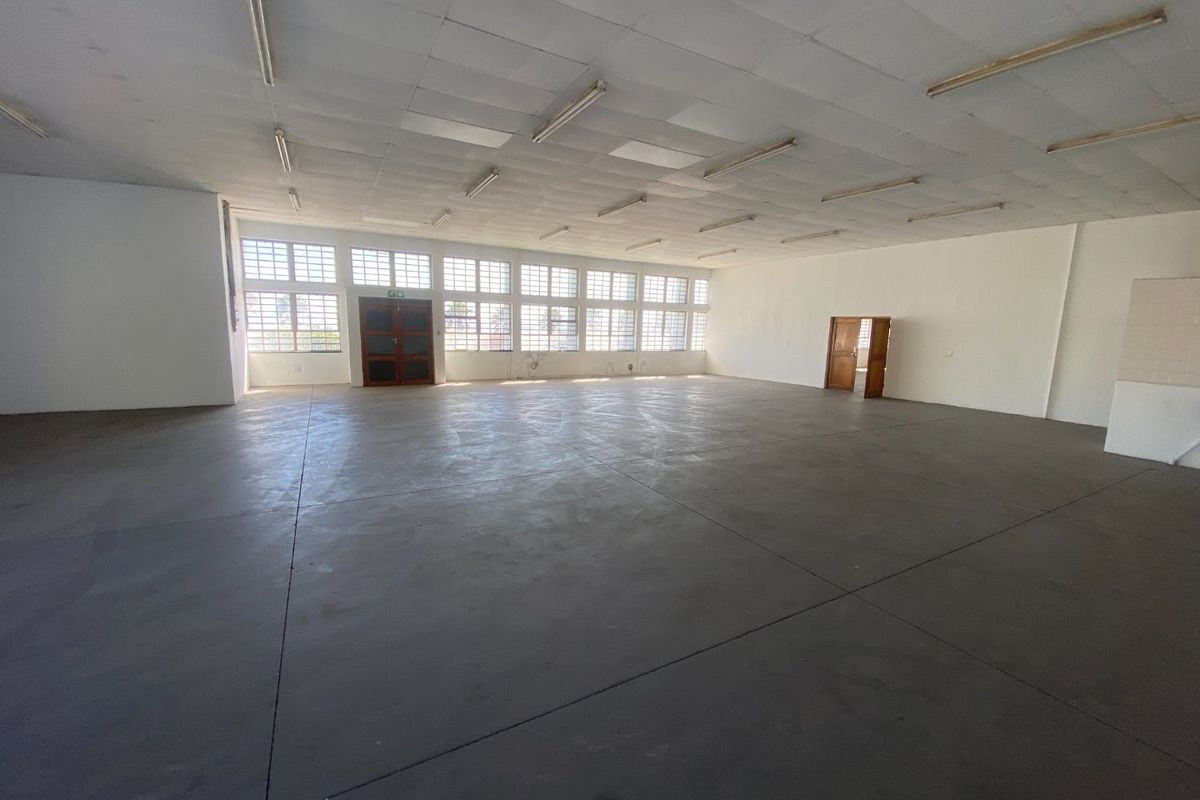 A spacious, open-plan industrial utility area featuring concrete flooring, a suspended ceiling with fluorescent lighting, and large multi-pane windows providing ample natural light.