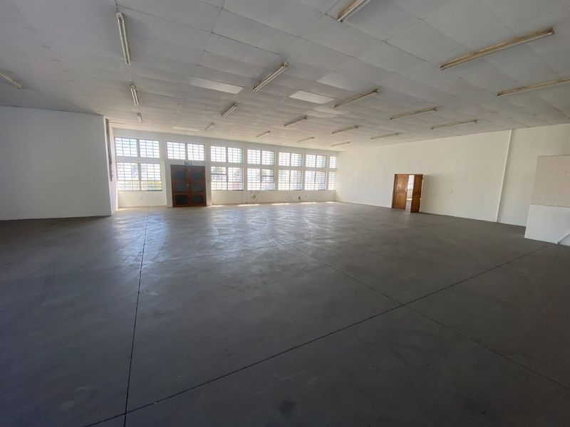 A spacious, open-plan industrial utility area featuring concrete flooring, a suspended ceiling with fluorescent lighting, and large multi-pane windows providing ample natural light.