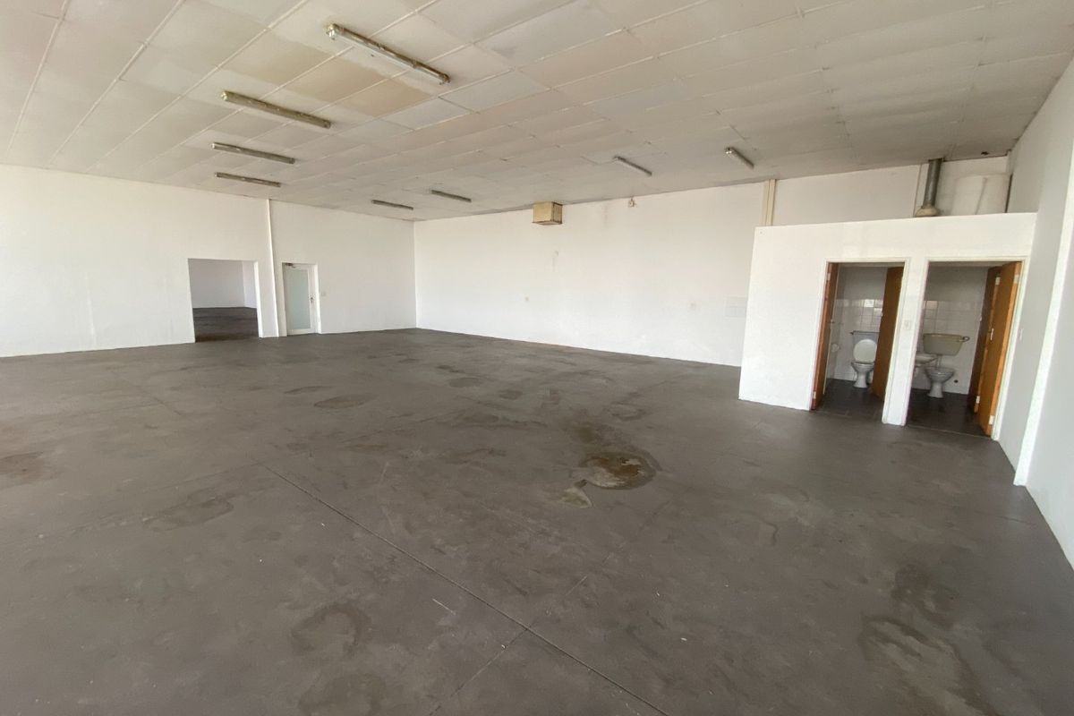 Spacious open-plan industrial unit featuring concrete flooring, suspended ceiling with fluorescent lighting, and two integrated toilet facilities.