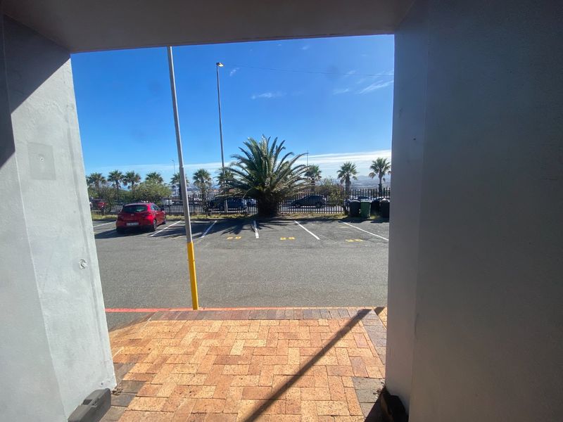 View from a covered entrance looking out onto a paved parking area with marked bays and security fencing.
