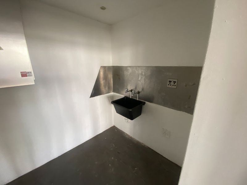 A functional utility or laundry area featuring a wall-mounted sink, metal splashback, and basic electrical infrastructure in an industrial setting.