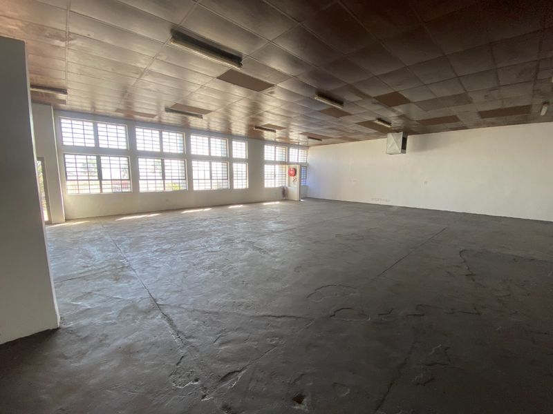 Spacious open-plan industrial unit featuring concrete flooring, large steel-framed windows for natural light, and a functional grid ceiling with overhead lighting.