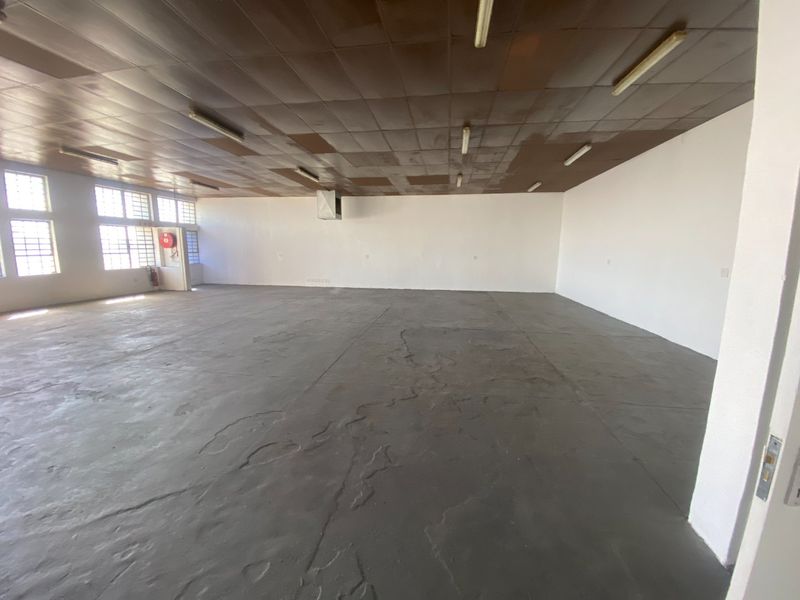 Spacious industrial utility area featuring concrete flooring, fluorescent lighting, and a tiled ceiling, suitable for storage or workshop use.
