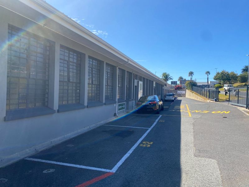 Exterior view of an industrial property featuring a paved driveway with marked parking bays and secure window grilles along the building facade.