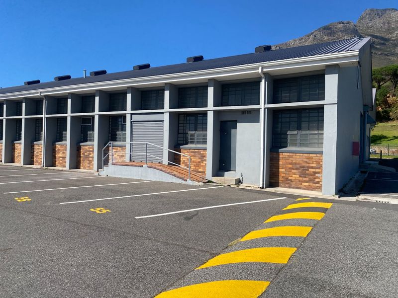 Exterior view of an industrial building featuring a metal roof, brick and concrete facade, security bars, and a dedicated concrete access ramp.