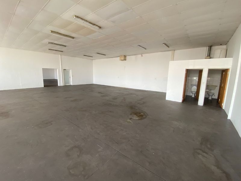 Spacious open-plan industrial unit featuring concrete flooring, suspended ceiling with fluorescent lighting, and two integrated toilet facilities.