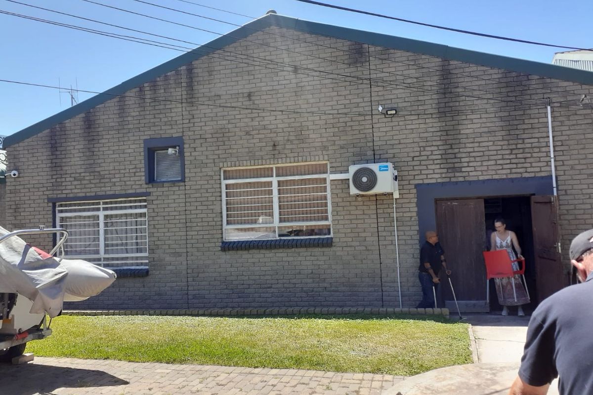 Rear view of a commercial brick building featuring security-barred windows, an external air conditioning unit, and a paved driveway area.