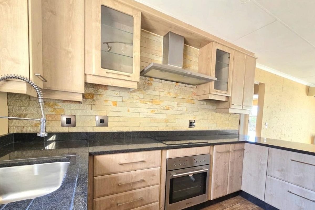 Modern kitchen featuring light wood cabinetry, granite countertops, a stone veneer backsplash, and integrated stainless steel appliances.