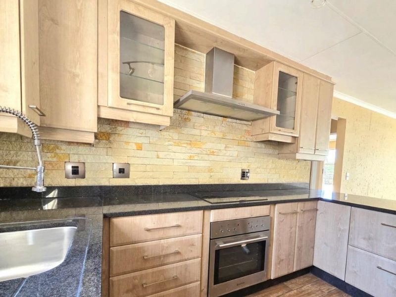 Modern kitchen featuring light wood cabinetry, granite countertops, a stone veneer backsplash, and integrated stainless steel appliances.